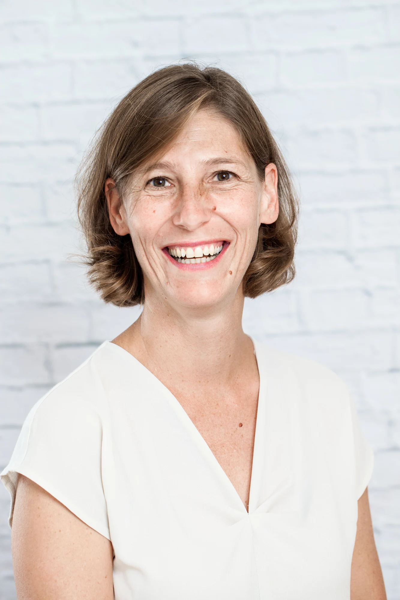 Natürlicher Business-Headshot einer lachenden Frau vor heller Wand
