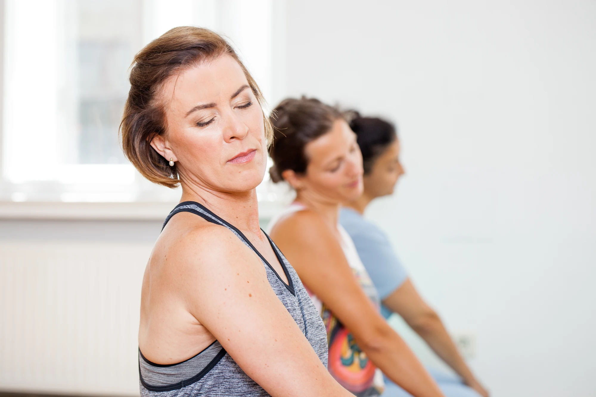 Yogatrainerin mit geschlossenen Augen, Teilnehmerinnen im Hintergrund